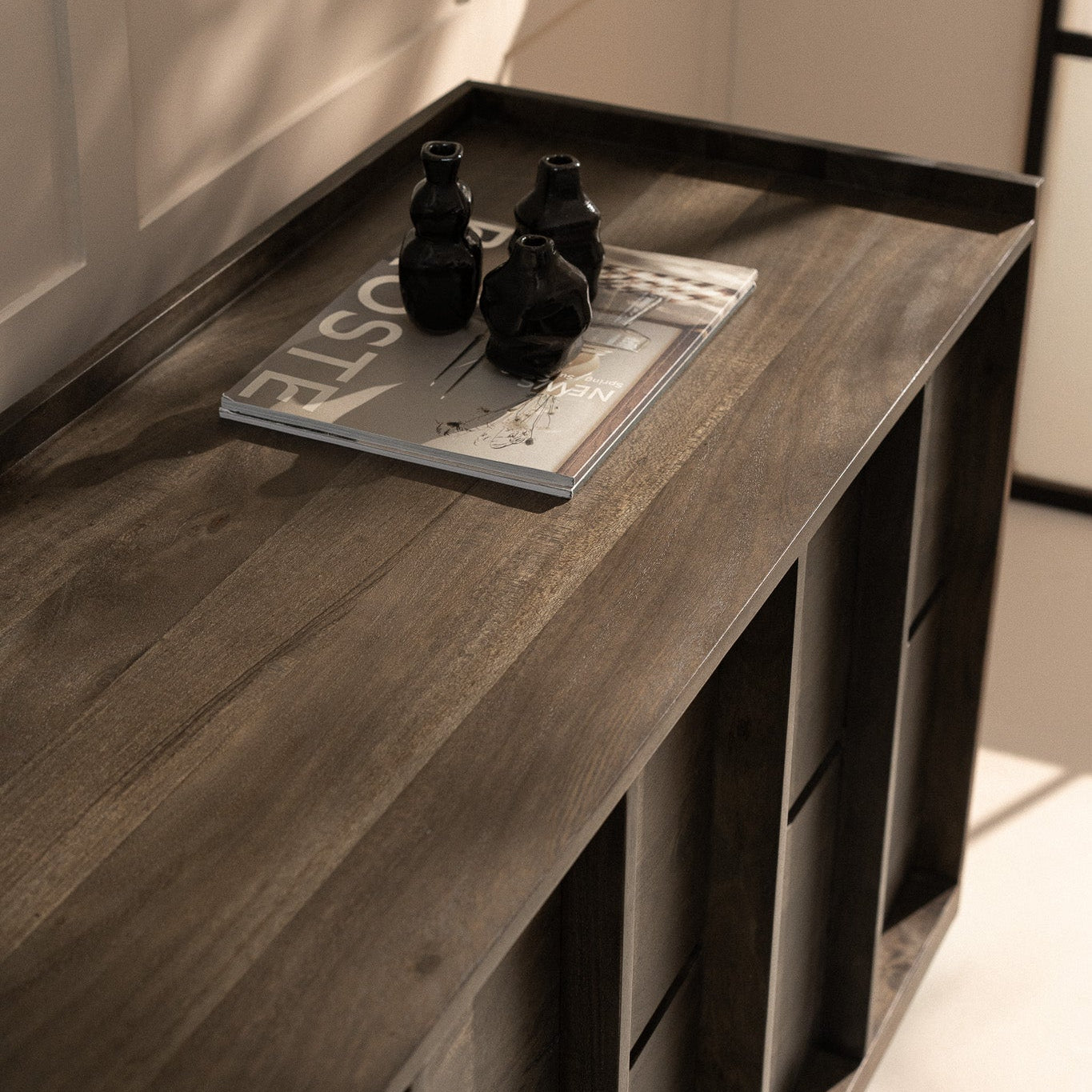 Decorative vases and a magazine on a dark wood sideboard.
