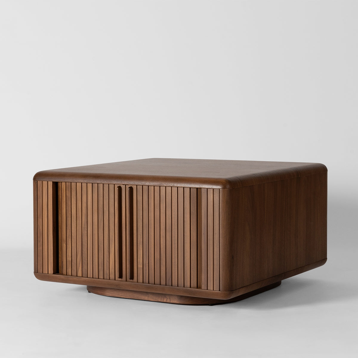 A mid-century modern wooden coffee table with a warm brown finish, featuring vertical slatted front doors and a rounded top, photographed on a light grey studio background.