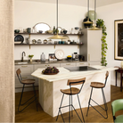 Modern kitchen with marble island, wooden bar stools, and shelves with decorative items.