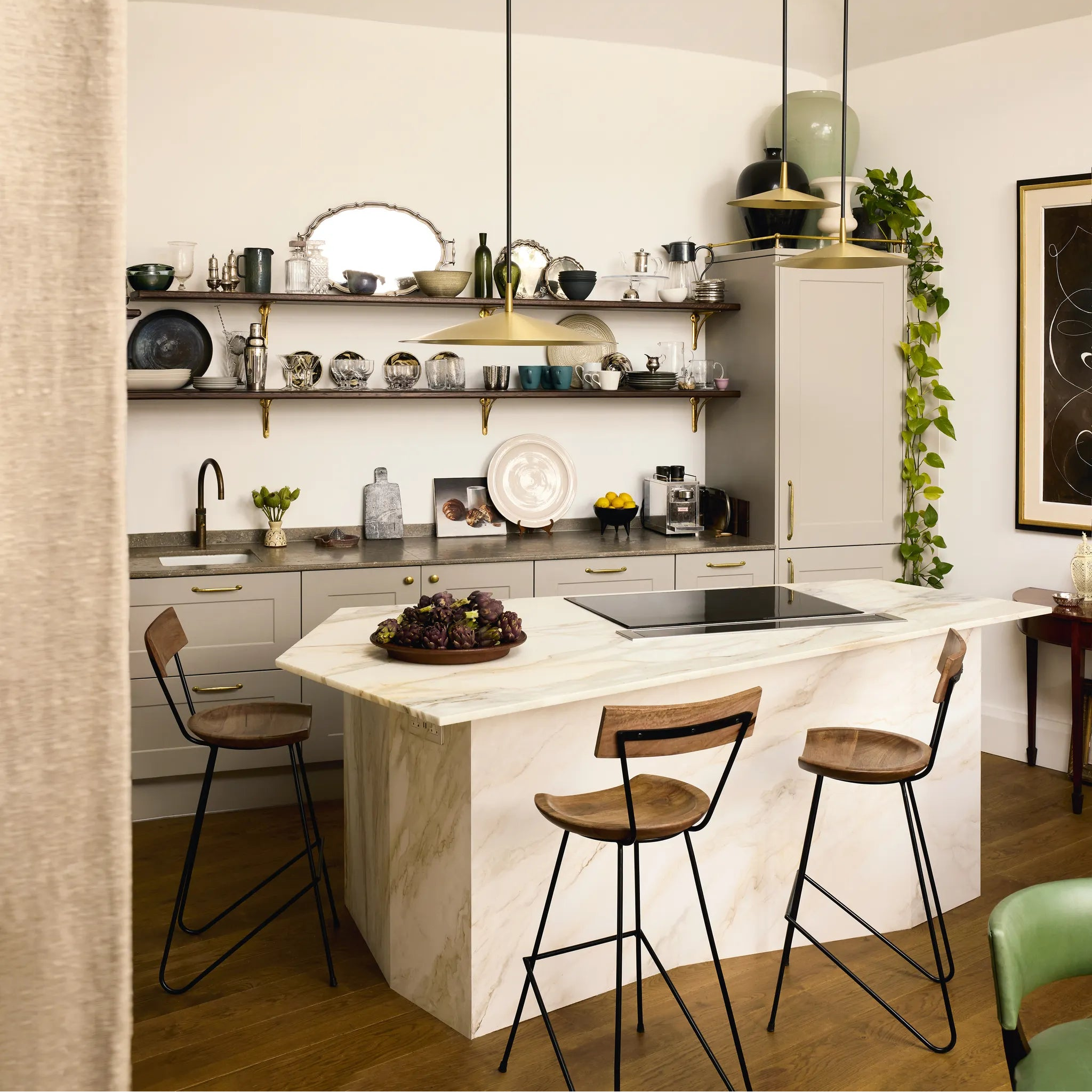 Modern kitchen with marble island, wooden bar stools, and shelves with decorative items.