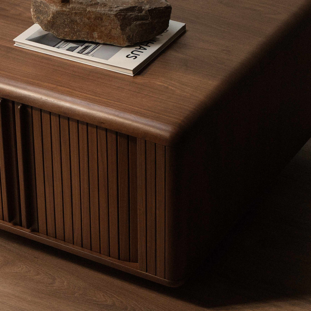 A mid-century modern wooden coffee table with a warm brown finish, featuring vertical slatted front doors and a rounded top.